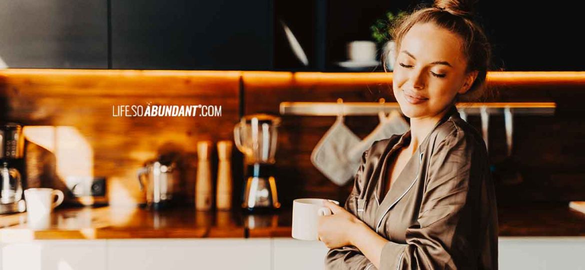 Morning Routine - Beautiful Young Happy Woman Standing In Kitchen Wearing Silk Pajamas - Life So Abundant®