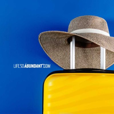 Luxury Travel Luggage - Bright yellow luxury luggage with fashionable vacation hat resting on the handle - Life So Abundant®